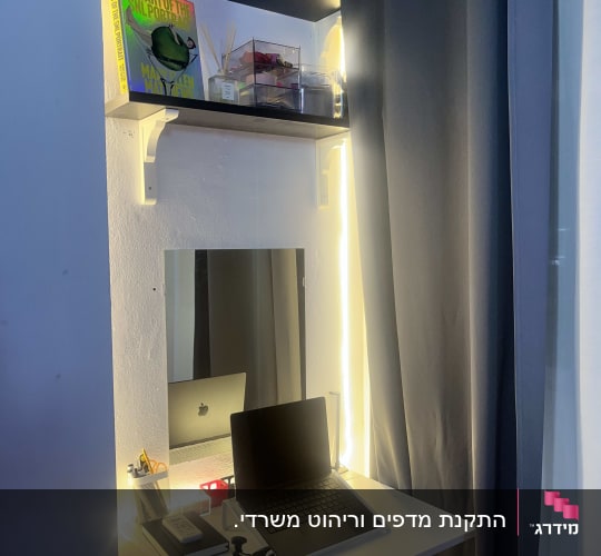 שולחן עבודה עם מחשב נייד ומדף עם ספרים וכלים.